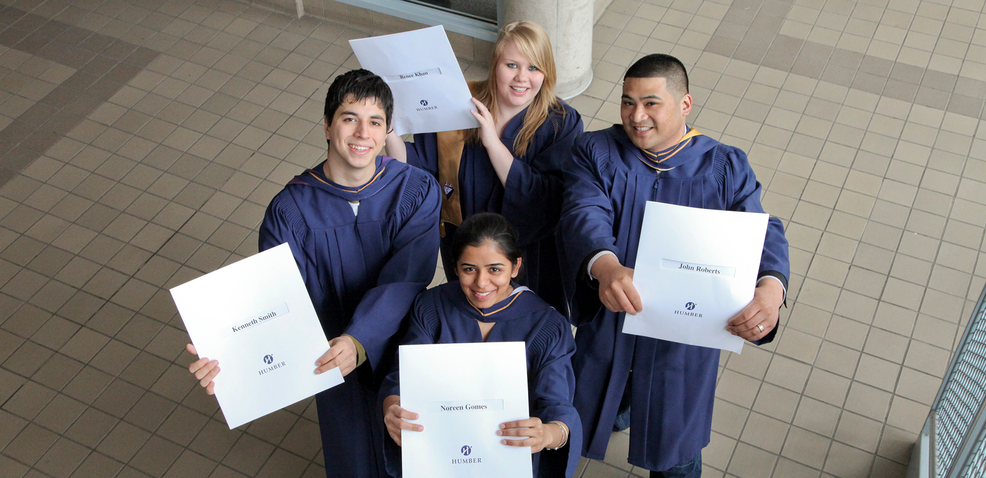Four students in graduation robes holding up their diplomas