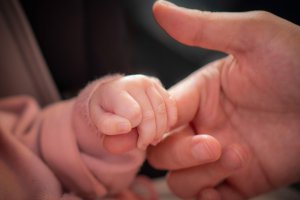 A baby holds an adult's finger in its hand.