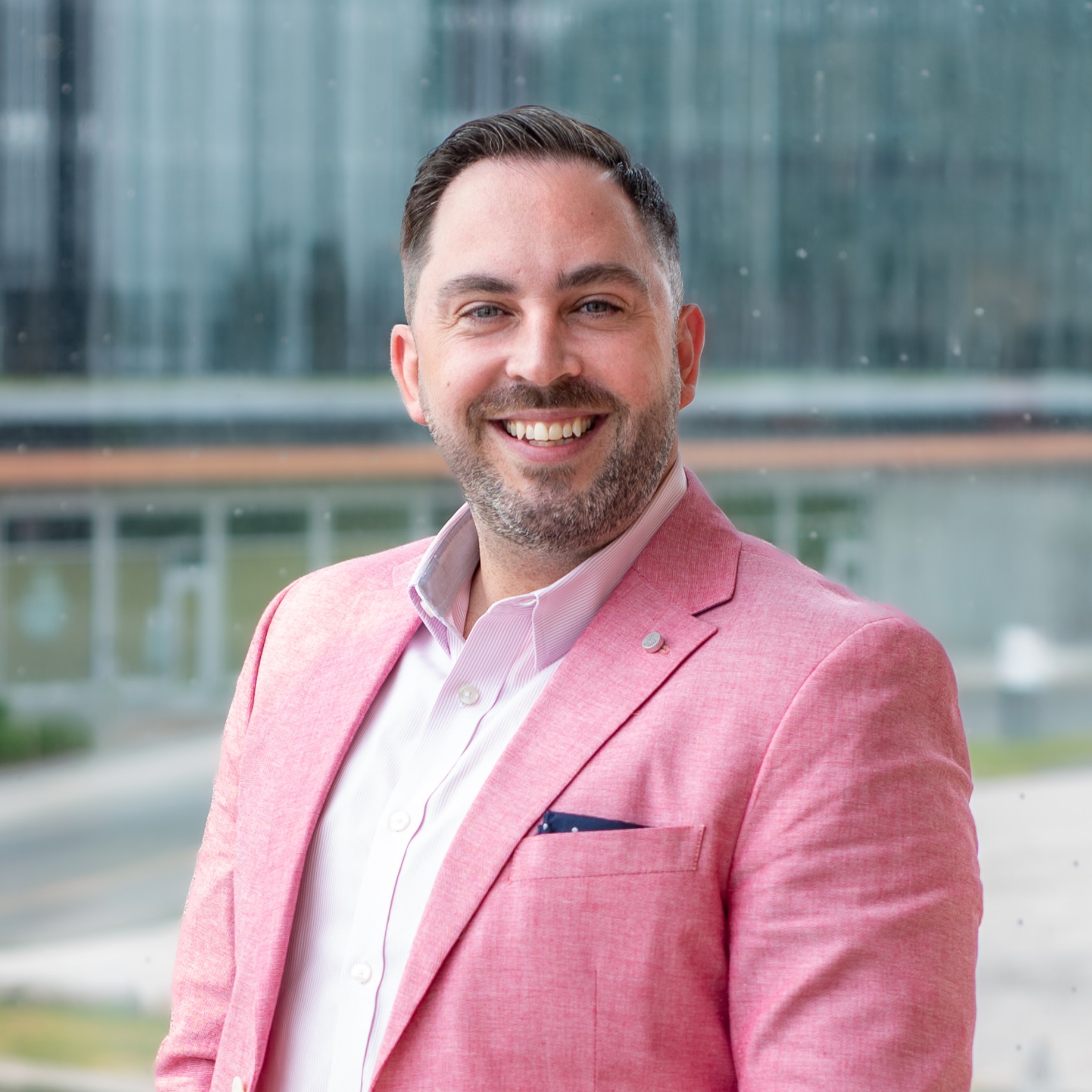 Tyler Charlebois, Director, Centres of Innovation Network & Partnership Development, smiles at the camera, wearing a pink sport jacket with a white shirt. 