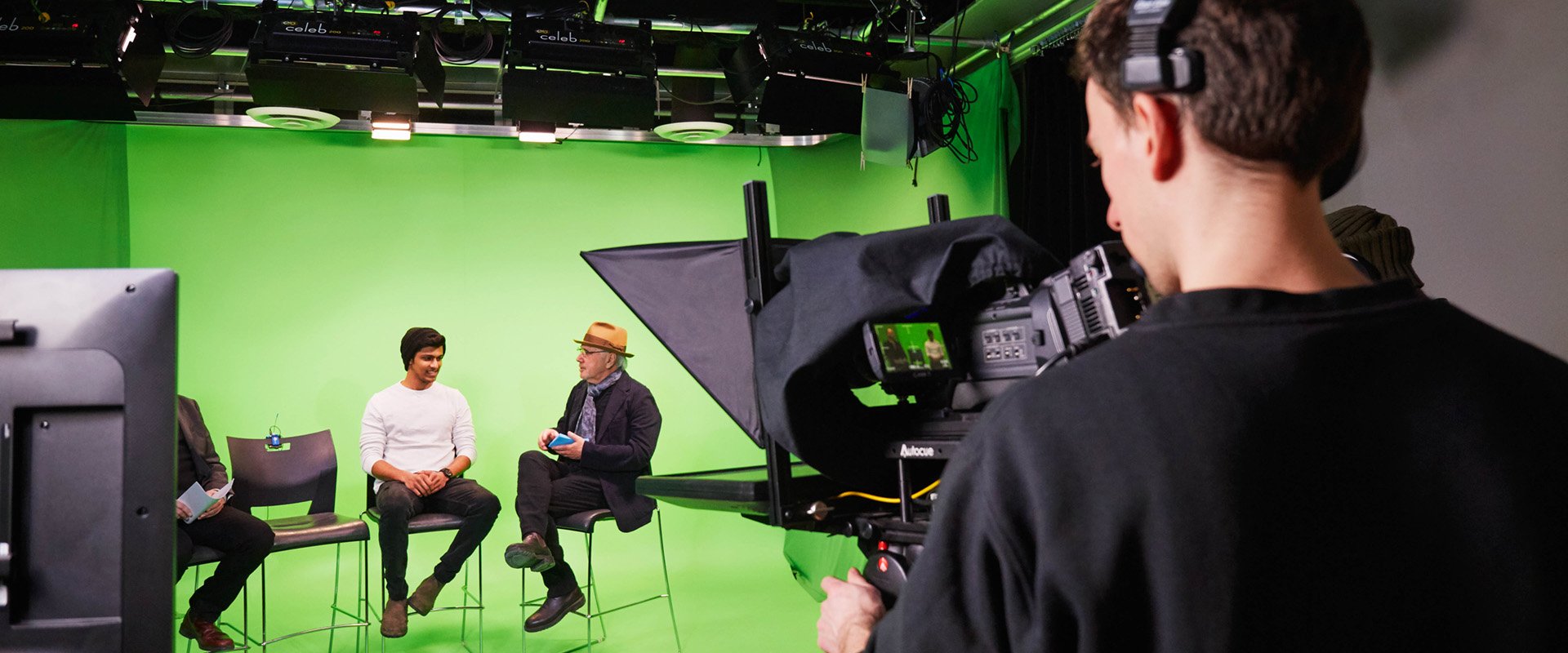 A camera man filming three people in front of a green screen.