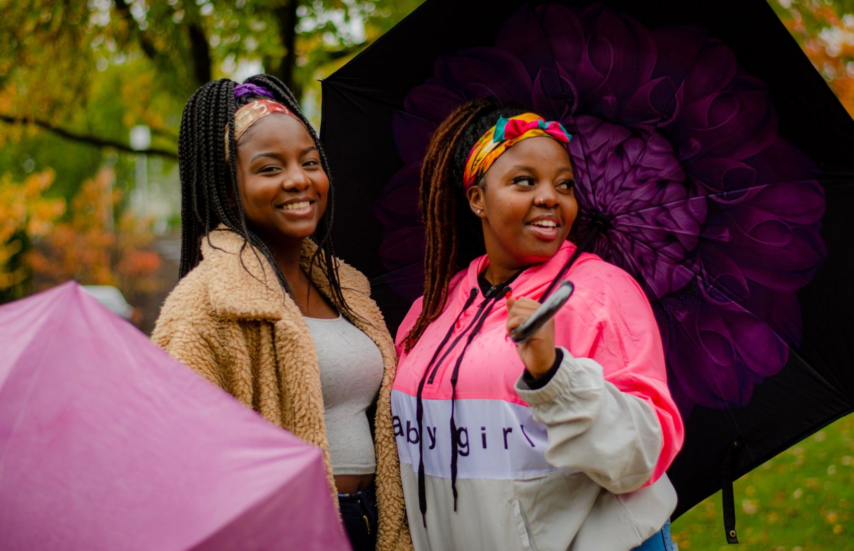 Two black females students outside in the fall, one is holding an umbrella