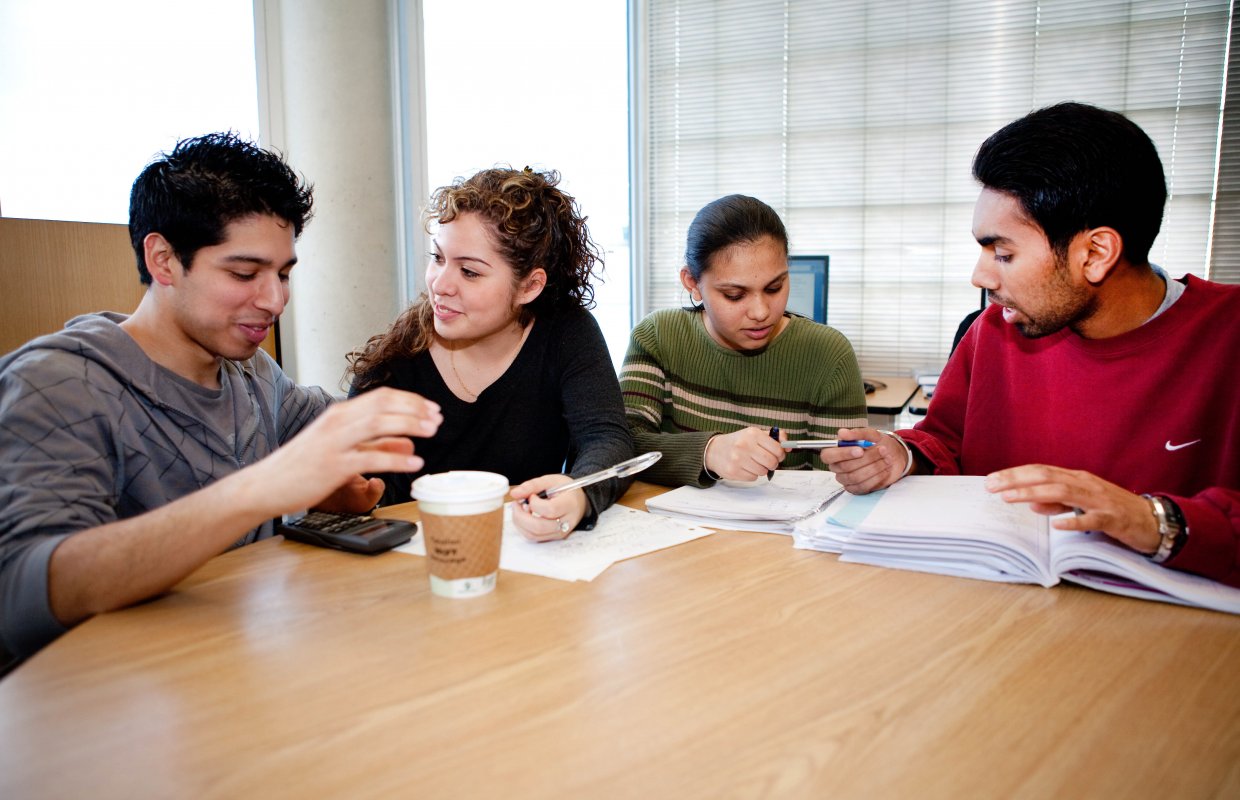 4 students writing and speaking to each other at a table
