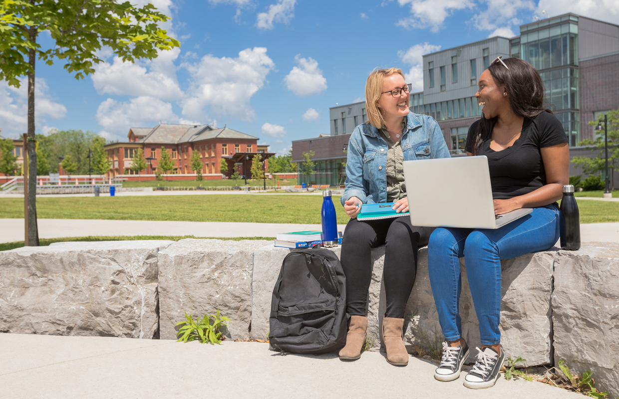 Two women sitting on a stone wall at Lakeshore campus