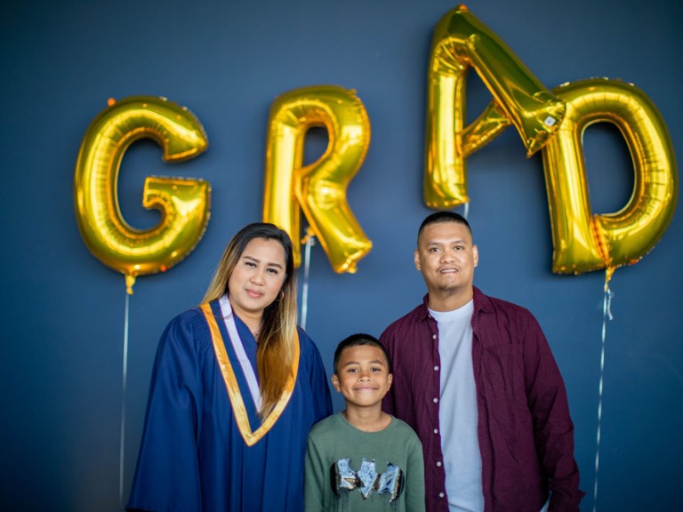 Humber graduate posing with their family in front of golden grad balloons