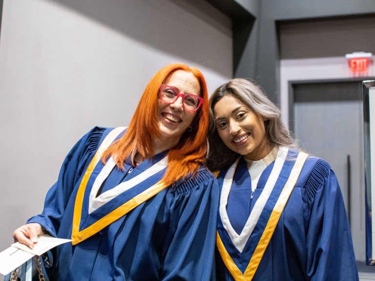 Two Humber graduates smiling with their heads leaning towards each other