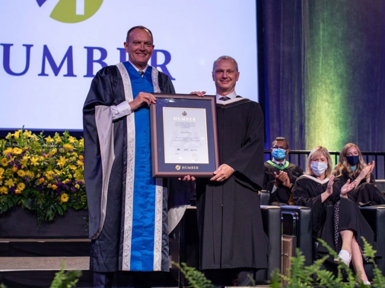 Former Humber president Chris Whitaker holding a framed document with another person