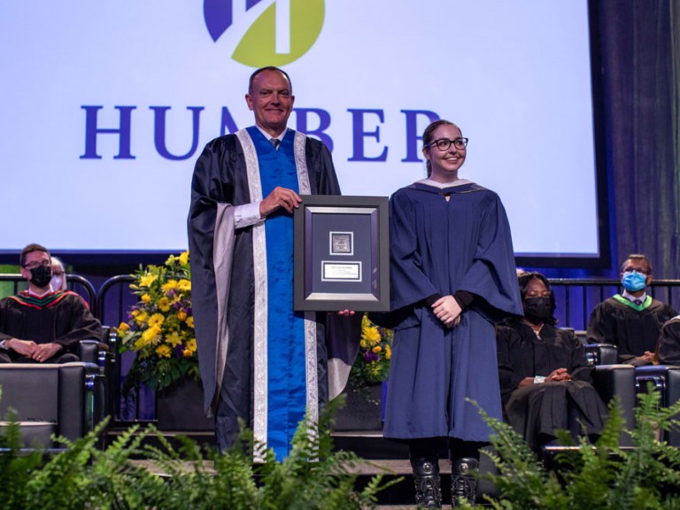 Former Humber president Chris Whitaker holding a framed document standing next to a graduate