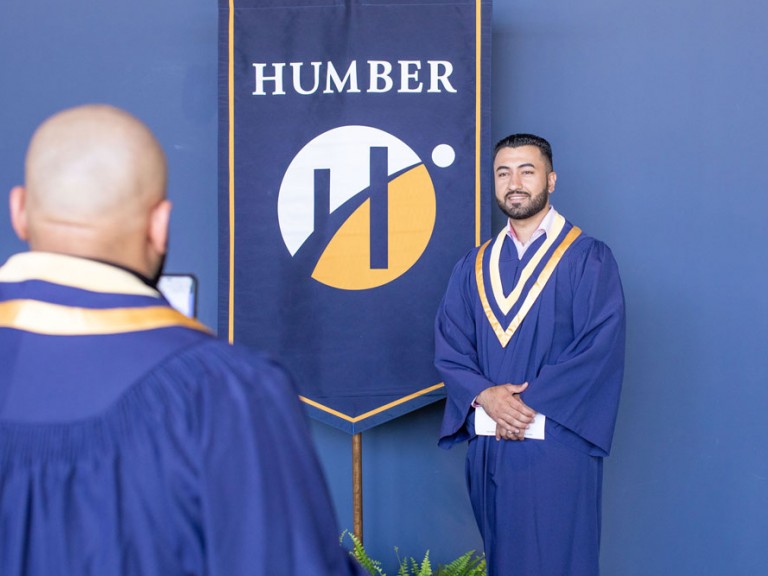 Humber graduate standing next to a Humber banner with their hands clasped