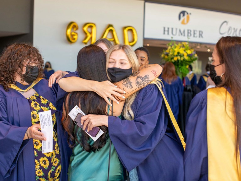 Humber graduate wearing a face mask hugging another person