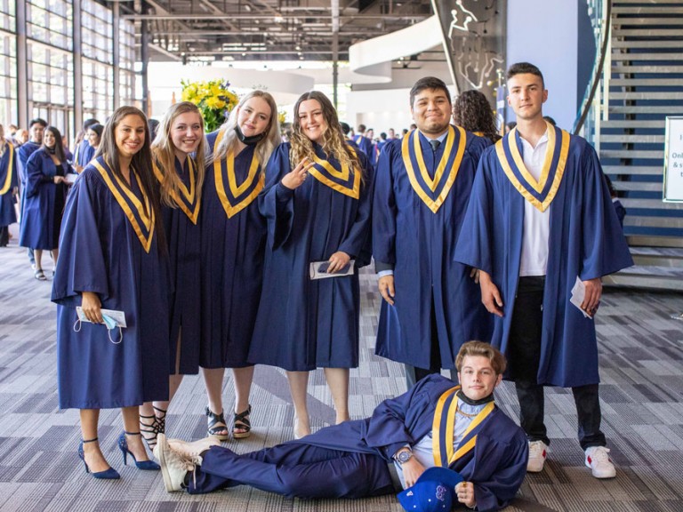 Group of six graduates smiling with one graduate posing on the floor in front