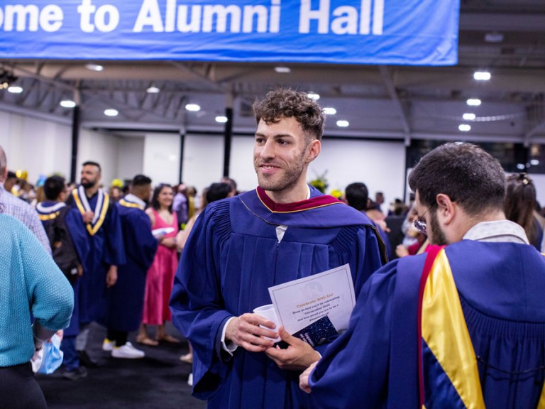Humber graduate standing with the Welcome to Alumni Hall banner in the background