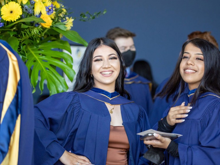Two graduates posing with plants behind them