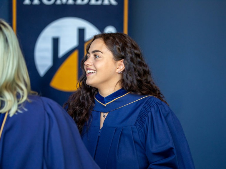 Graduate smiling in front of the Humber Banner