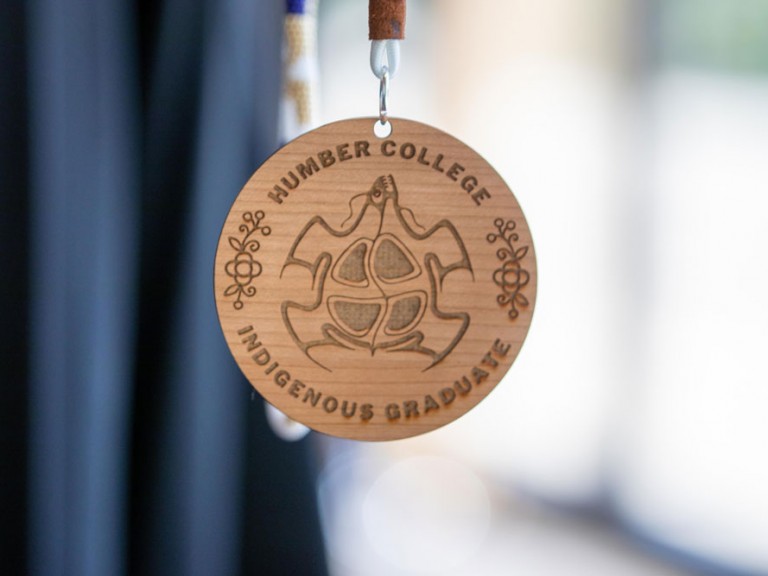 Closeup of wooden badge with laser cut words: Humber College Indigenous Graduate