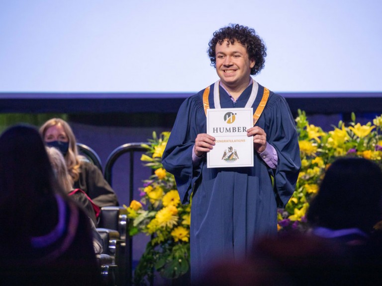 Graduate on stage holding a document that reads congratulations