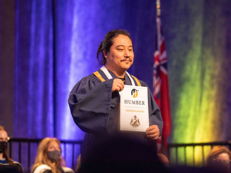 Humber graduate on stage smiling with their document