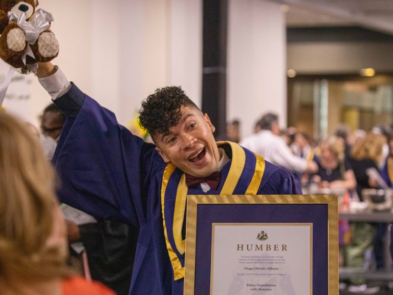 Humber graduate with a teddy bear in their raised hand
