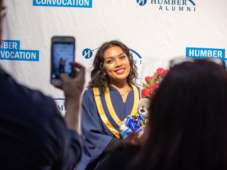 Person taking cell phone photos of a graduate in front of the Humber Convocation wall