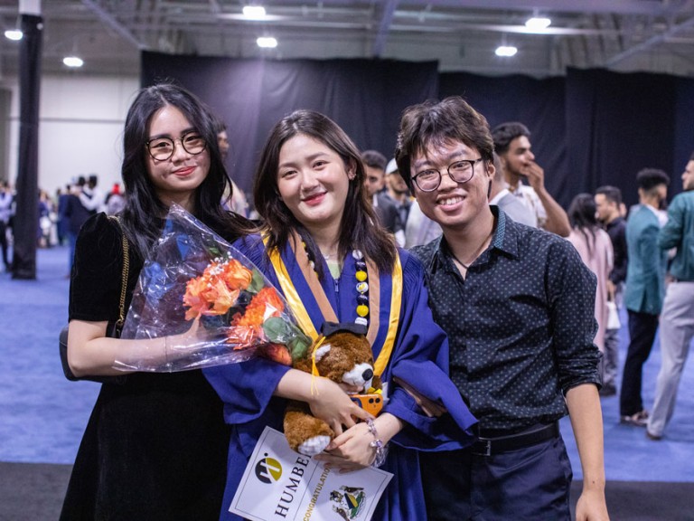 Three people smiling and holding flowers at Humber Graduation