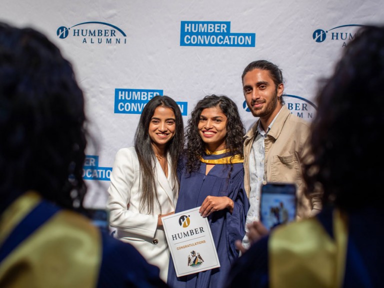 Three people in front of Humber Convocation wall