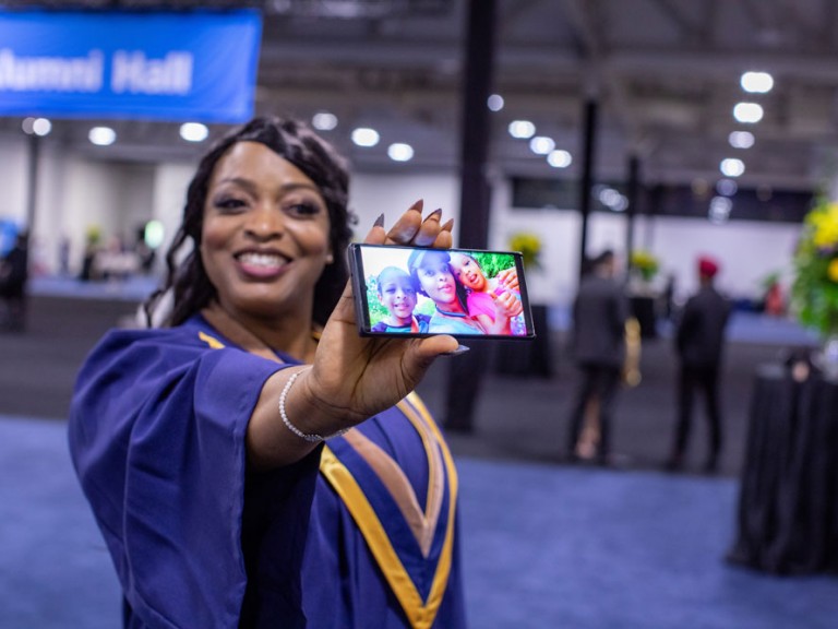 Humber Graduate holding cell phone photo up of children