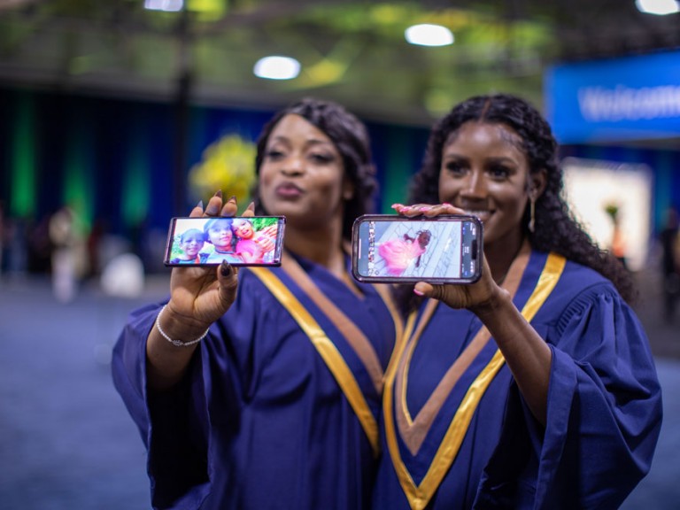 Two Humber Graduates holding phones up of children