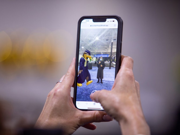 Phone taking picture of Humber Mascot with Graduate