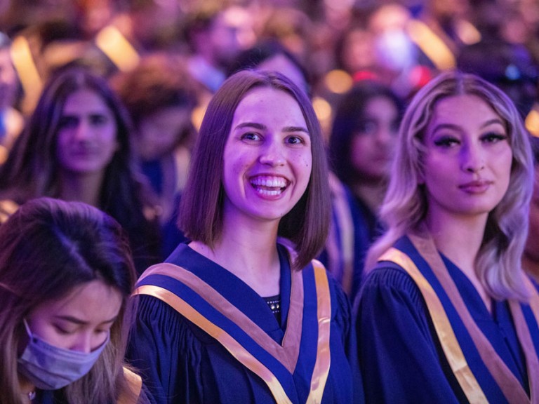 Person with shoulder length hair smiling at camera during Commencement ceremony