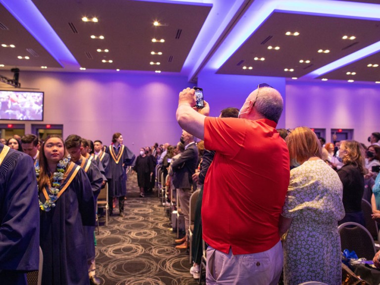 ceremony attendee takes photo of graduate procession