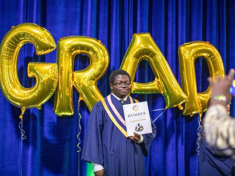 graduate posing for photo in front of golden grad letter balloons