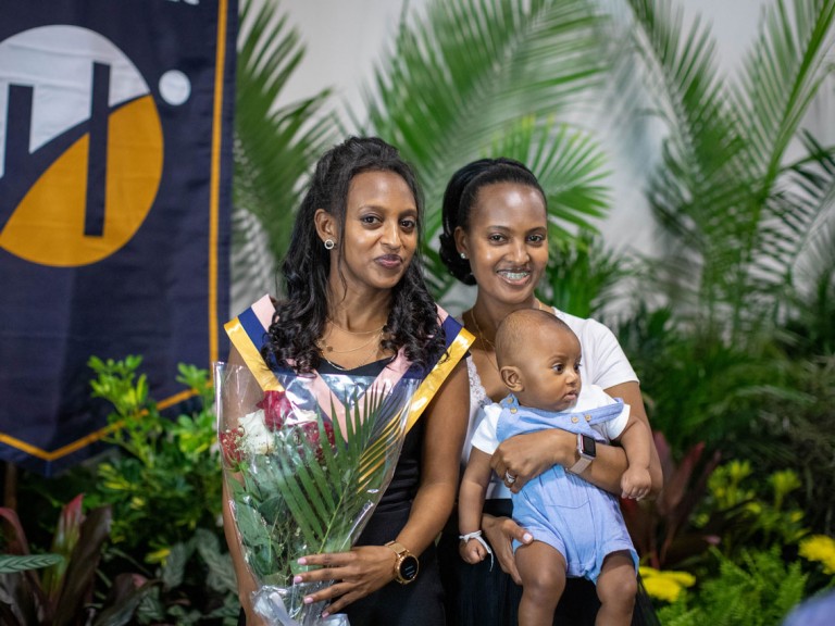 Humber graduate with family member holding baby in front of Humber banner
