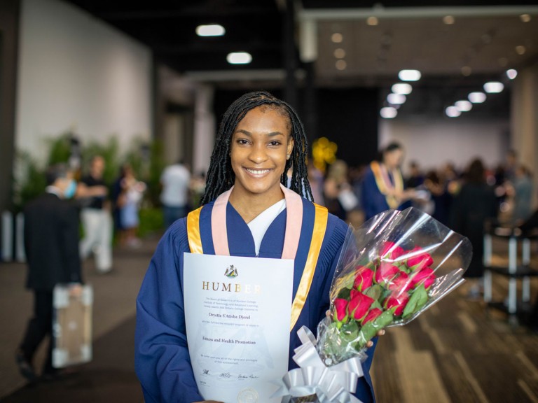 Humber graduate holding diploma and roses smiling