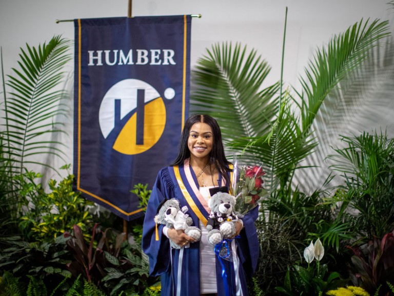 graduate with teddy bears in front of Humber banner