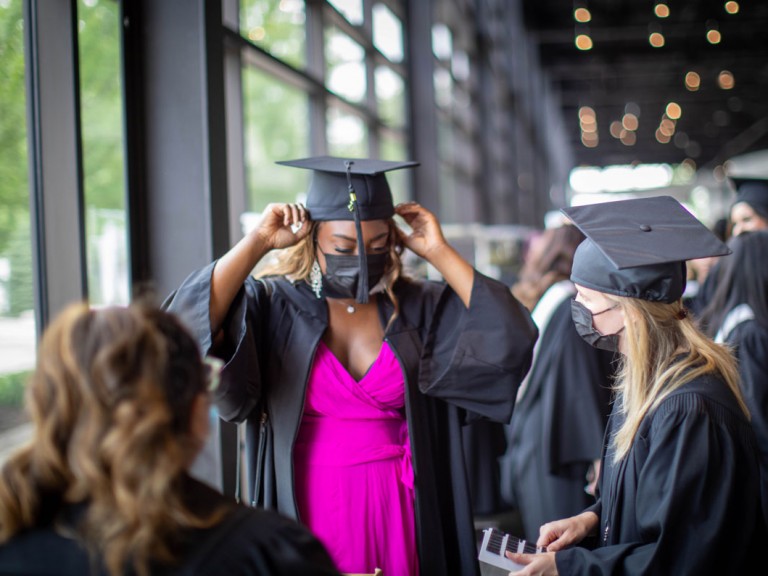 Humber graduate in black gown and cap puts on face mask