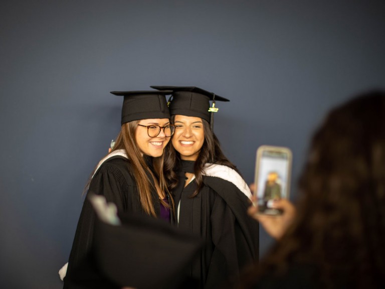 two graduates in black gowns and caps smile for photo