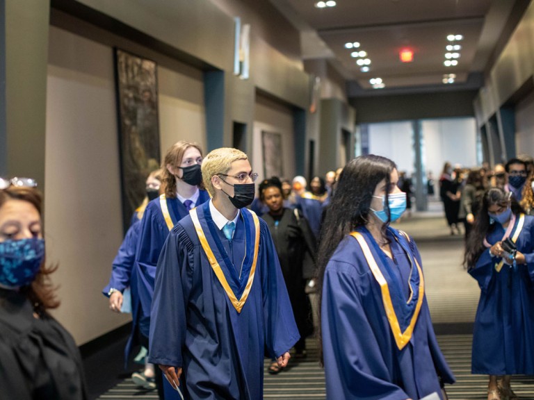 graduates in face masks proceed into ceremony hall