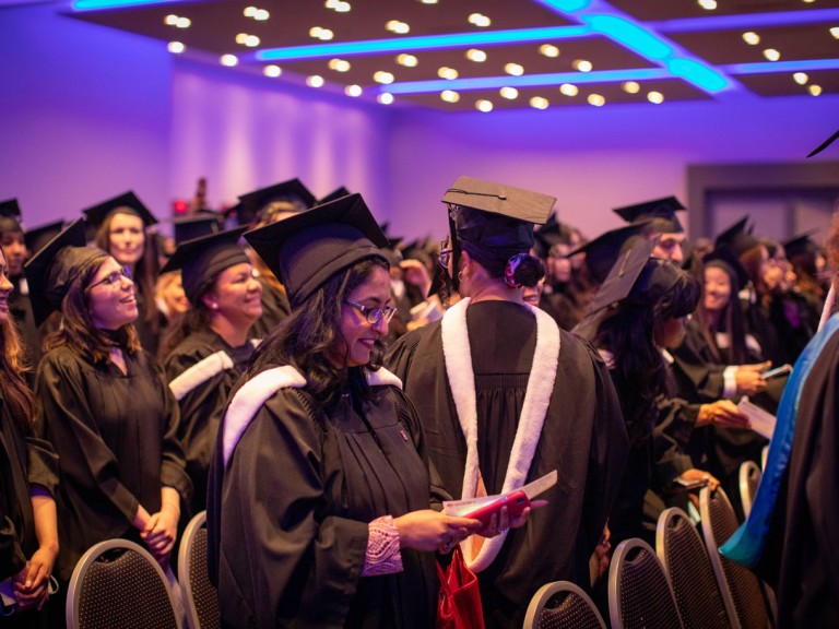 graduates in black caps standing amongst seats