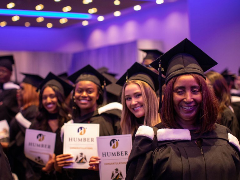 Humber graduates in black caps hold up congratulations paper