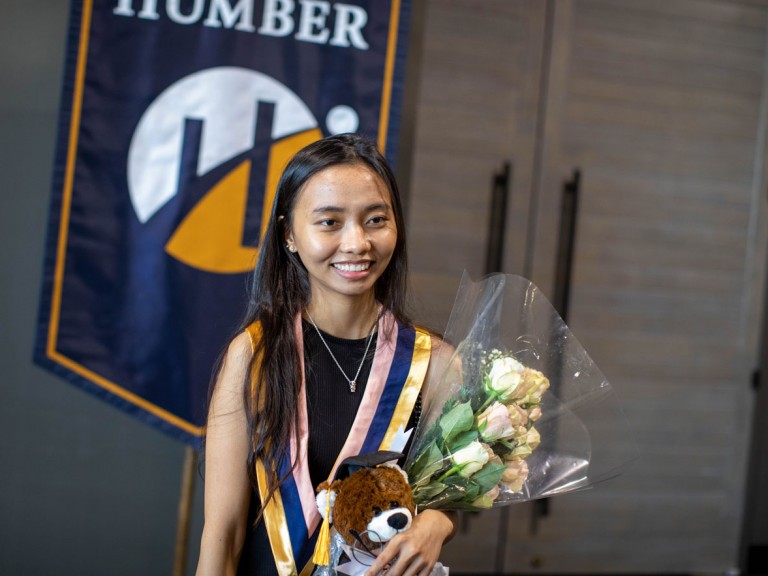 Humber graduate with white roses in front of Humber banner