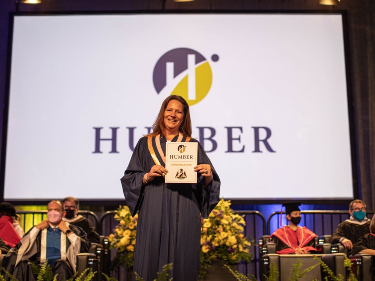 New graduate holding diploma and smiling on stage