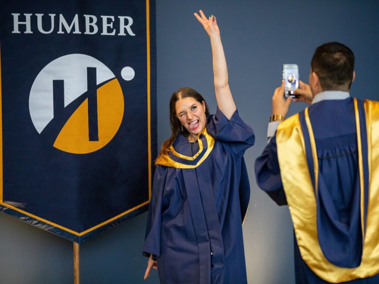 Grad taking picture of another grad in front of Humber banner