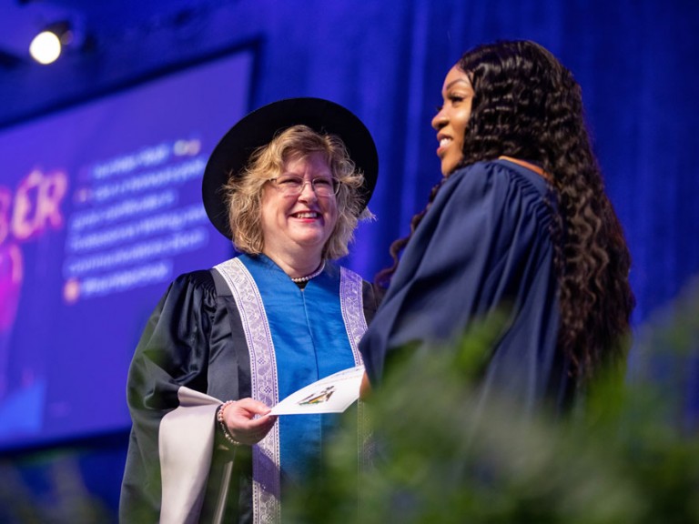 Humber president smiling and presenting certificate to graduate