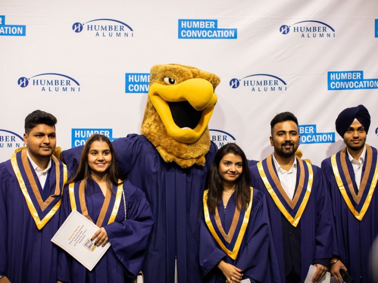 Five graduates posing with Humber mascot