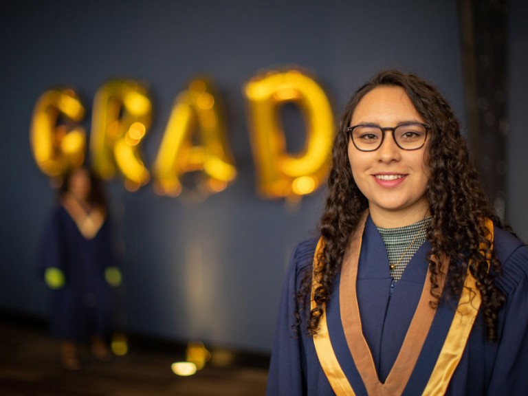 Grad posing with gold GRAD balloons in background