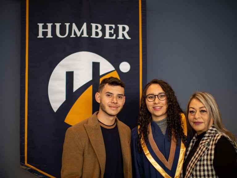 Grad posing with two people in front of Humber banner