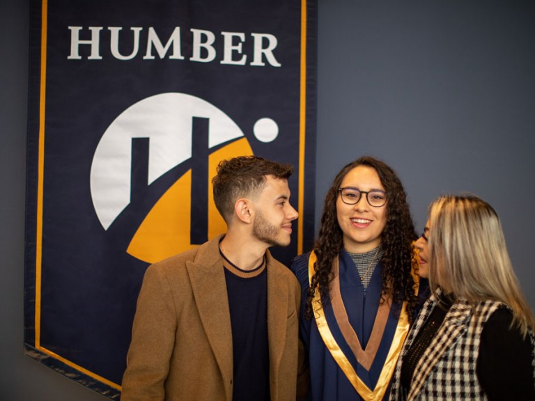 Grad posing with two people in front of Humber banner
