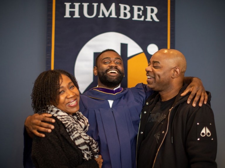 Grad smiling with parents in front of Humber banner