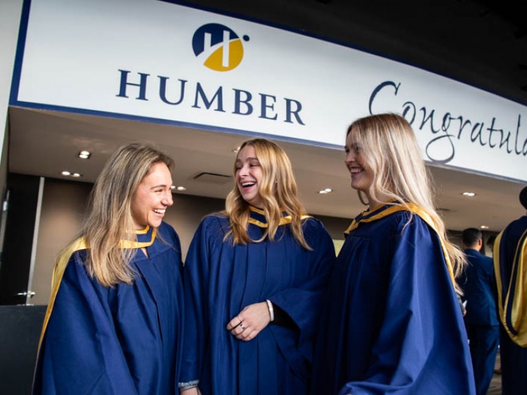 Three graduates smiling under Humber congratulations sign