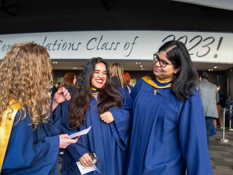 Three graduates smiling with Humber class of 2023 sign in background