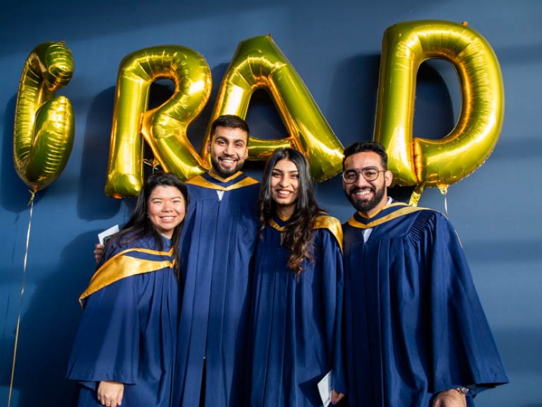 Four graduates pose under golden GRAD balloons